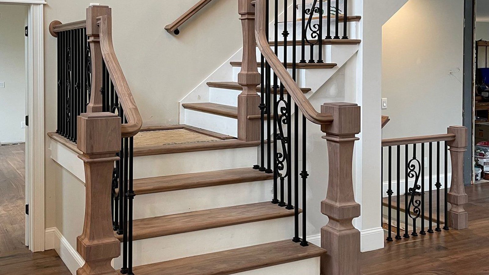Custom wood staircase with white risers, unfinished handrails and newel posts, and decorative black iron balusters.